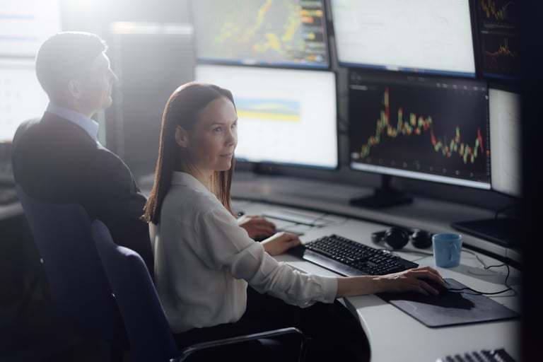 Two people in front of multiple screens watching some stock market.